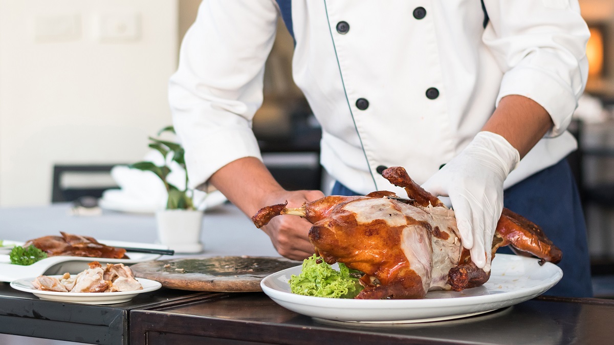 Chef preparing Chinese Peking Duck on dishes for food serving on restaurant table